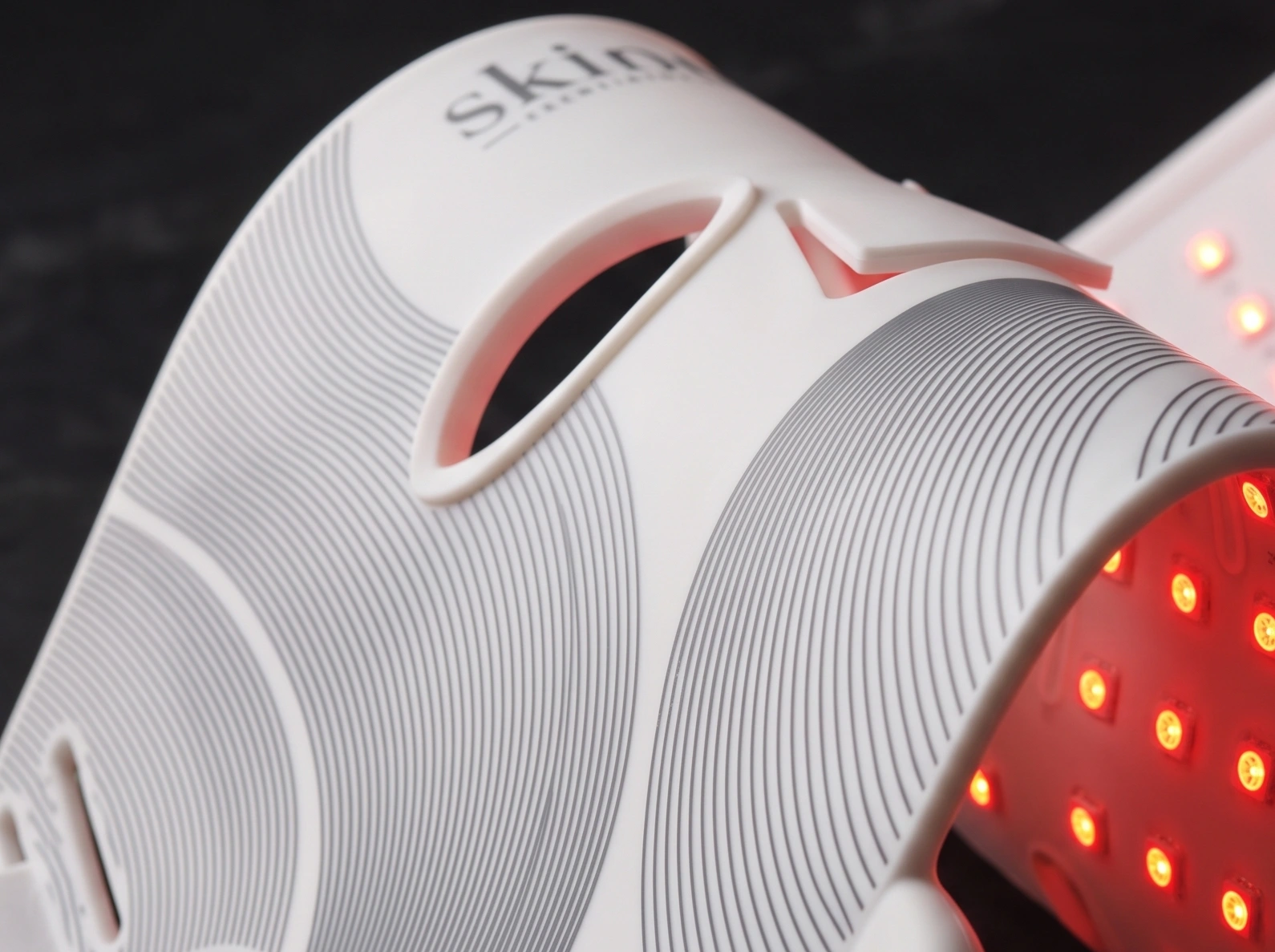 Nærbilde av Skinora Radiance Face — silikonmaske med LED-rutenett, holdt i hånden.